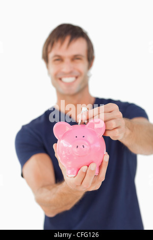 Junger Mann, indem Notizen in ein Sparschwein Stockfoto