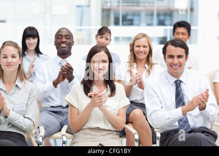 Eine Gruppe von lächelnden Kollegen applaudierten als She Sit mit einander Stockfoto