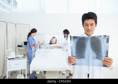 Blick auf eine Röntgen-Untersuchung, während seine Kollegen einen Patienten untersuchen Arzt Stockfoto