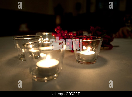 Kerzen leuchten Stechpalme Beeren auf einem Tisch bei einer Hochzeit im Dunkeln. Stockfoto