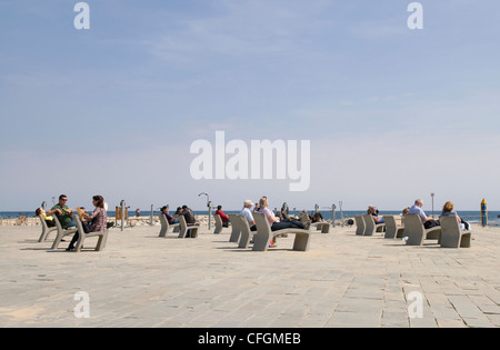 Menschen sitzen entspannt auf moderne Beton Stühle im Vordergrund des Meeres in Barcelona mit öffentlichen Fitnessgeräten im Hintergrund Stockfoto