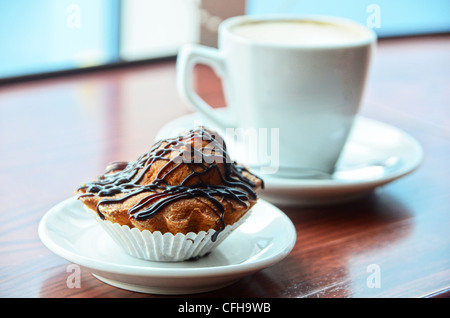 Schokoladen-Muffins mit und Kaffeetasse auf orange Tisch Stockfoto