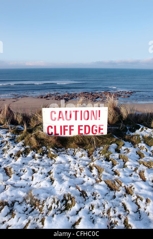 ein rotes Vorsicht Zeichen auf einer Klippe im tief verschneiten ballybunion Stockfoto