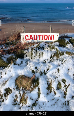 ein rotes Vorsicht Zeichen auf einer Klippe im tief verschneiten ballybunion Stockfoto