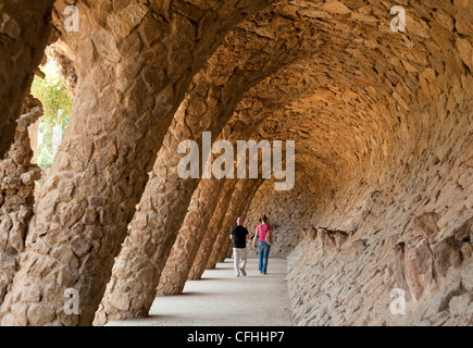 Ein paar Touristen Fuß unter der gewölbten geformten terrassenförmig angelegten Stein Gehwege im Park Güell, Barcelona Stockfoto