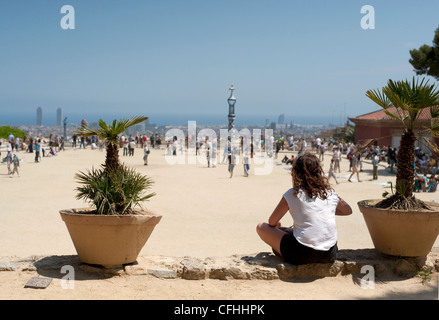 Ein junges Mädchen in einem weißen t-Shirt sitzt die Touristen auf der großen Terrasse im Park Güell Barcelona in der Ferne beobachtet. Stockfoto