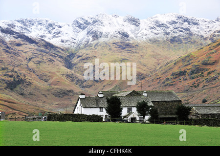 Bauernhaus mit Schnee Langdale Pikes im Hintergrund am Ende des Langdale Valley, Great Langdale, Lake District, Cumbria, England, Großbritannien begrenzt Stockfoto