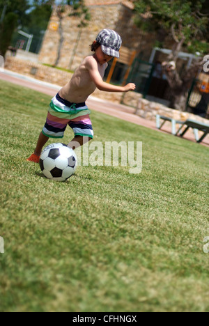 Jungen Fußball spielen - läuft ein fünf Jahre alter Junge mit einem Fußball auf dem Rasen im Sommer Stockfoto