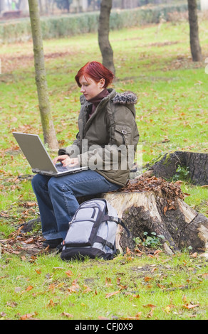 Rothaarige Mädchen arbeiten am Computer in einem Park im Herbst. Stockfoto
