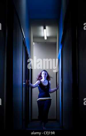 eine einzelner junge rote kurzhaarige Frau Mädchen allein Angst drinnen Angst besorgt weglaufen in Angst auf einem dunklen engen Korridor in einem Gebäude Stockfoto
