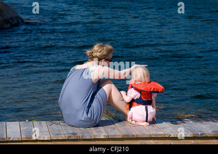 Mutter und Kind trägt Schwimmweste sitzen auf der Mole mit Blick auf Meer Stockfoto