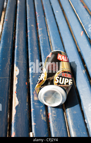 Einen leeren und halb zerdrückte Bierdose liegt auf einem blauen hölzernen Sitz einer Park Unterkunft wo ist wurde von den Trinker verlassen. Stockfoto