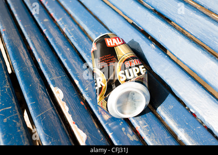 Einen leeren und halb zerdrückte Bierdose liegt auf einem blauen hölzernen Sitz einer Park Unterkunft wo ist wurde von den Trinker verlassen. Stockfoto