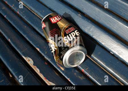 Einen leeren und halb zerdrückte Bierdose liegt auf einem blauen hölzernen Sitz einer Park Unterkunft wo ist wurde von den Trinker verlassen. Stockfoto