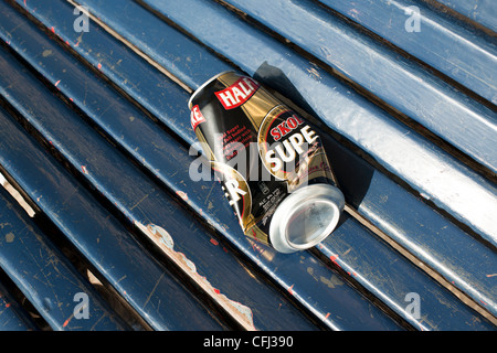 Einen leeren und halb zerdrückte Bierdose liegt auf einem blauen hölzernen Sitz einer Park Unterkunft wo ist wurde von den Trinker verlassen. Stockfoto