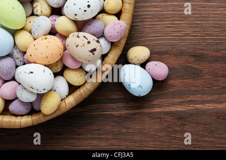 Still-Leben Foto gefleckte Süßigkeiten bedeckt Schokoladeneier in einem Weidenkorb auf einem rustikalen Holztisch. Stockfoto