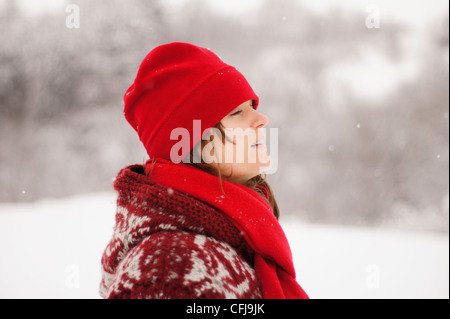 Schöne junge Mädchen mit roter Mütze und Schal genießen den fallenden Winterschnee Stockfoto