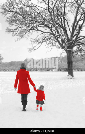 Winter Weihnachtskarte Schnee Szene Mutter & Tochter rote Mäntel und Gummistiefel mit Bäumen Hand in hand mit hand Stockfoto