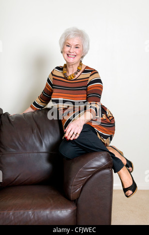 Attraktive ältere Dame saß am Rand der Ledersofa lächelnd und entspannt suchen Stockfoto
