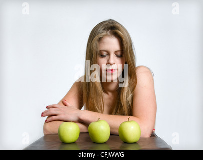 Attraktive junge Frau kaukasischen saß Blick auf drei Äpfel vor ihr Stockfoto