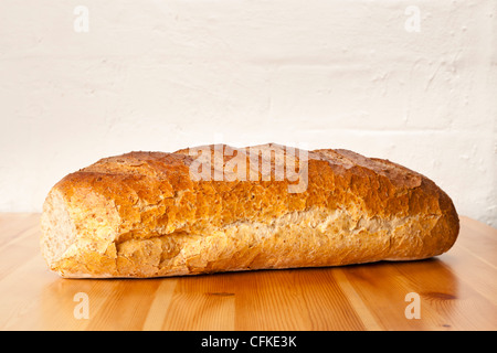 Laib braun Vollkornbrot auf einen hölzernen Tisch gegen eine bemalte Mauer Stockfoto