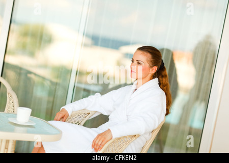 Ernsthafte hübsche Frau im Bademantel auf Terrasse mit Kaffee am Tisch sitzen Stockfoto