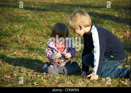 Kinder Bruder und kleine Schwester sitzen im Bereich des Grases Stockfoto