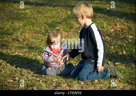 Kinder Bruder und kleine Schwester sitzen im Bereich des Grases Stockfoto