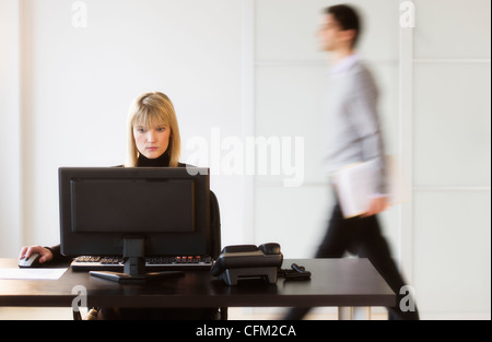 USA, New Jersey, Jersey City, Geschäftsfrau, die Arbeiten am Computer, Geschäftsmann, die im Hintergrund laufen Stockfoto