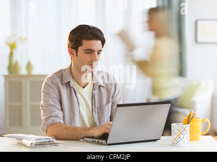 USA, New Jersey, Jersey City, Mann arbeitet am Laptop zu Hause, Frau im Hintergrund Stockfoto