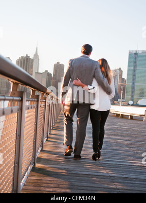 USA, New York, Long Island City, Rückansicht des jungen Paares zu Fuß auf der Promenade, im Hintergrund die Skyline von Manhattan Stockfoto