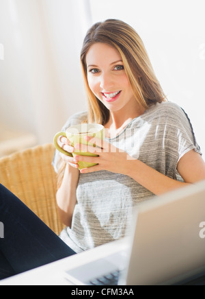 Porträt der jungen Frau mit Laptop und Becher, Jersey City, New Jersey, USA Stockfoto
