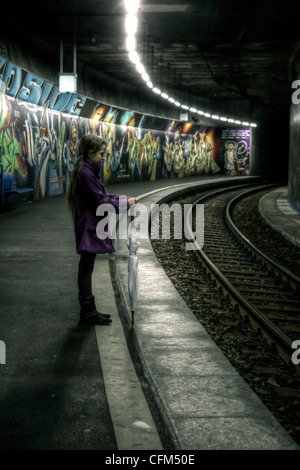 Mädchen mit Regenschirm steht auf einer Plattform zu einer u-Bahnstation mit Graffiti und wartet. Stockfoto