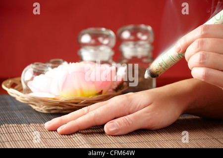 TCM-Traditionelle chinesische Medizin. Hand, die Anwendung von Moxa Stick Therapie, natürlicher Kräutern in Gläsern im Hintergrund Stockfoto