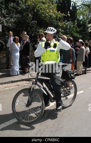 Ein Polizist auf seinem Fahrrad mit seinem Mobiltelefon während im Dienst, Großbritannien Stockfoto