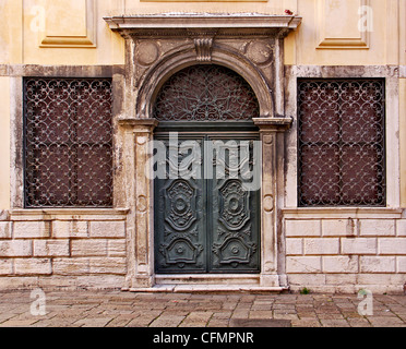 Eine grüne verzierte Holztür flankiert von zwei Eisen geriebener Windows in der alten Ghetto von Venedig Stockfoto