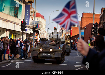 Truppen in gepanzerten Fahrzeugen vorbeifahren High Street Läden während einer Parade Royal Yeomanry, winken Zuschauern Union Jack-Flaggen Stockfoto