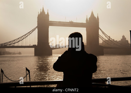 die Silhouette eines Touristen mit dem Fotografieren der Tower Bridge in der Dämmerung Stockfoto