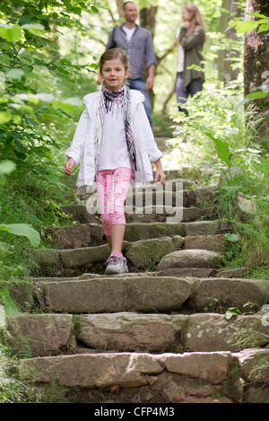 Mädchen zu Fuß hinunter Steinstufen in Wäldern, Eltern im Hintergrund Stockfoto