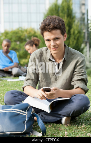 Junger Mann mit Handy, Freunde im Hintergrund, Porträt Stockfoto