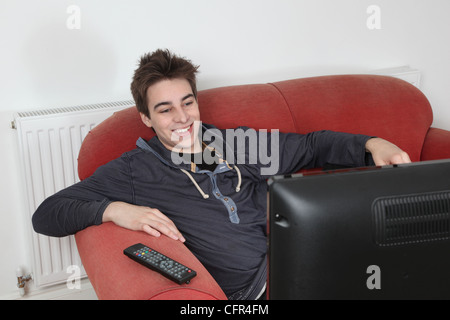 Junger Mann lächelnd vor dem Fernseher auf eigene Faust. Stockfoto