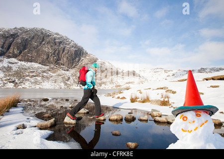 Frau Hill Wanderer durch eine gefrorene scheut Tarn in die saisonabhängige, Lake District, Großbritannien Stockfoto