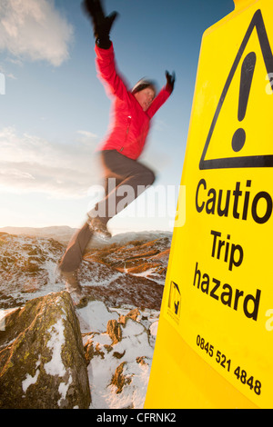 Ein Bergsteiger auf Todd Crag Gipfel im Lake District, UK, bei Dämmerung und Reise-Gefahr-Zeichen. Stockfoto