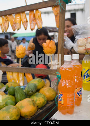 Antigua, Guatemala. 23.03.07 geschnittene frisch Früchte auf Sticks für Verkauf Kontrast mit westlichen alkoholfreie Getränke im Markt Stadt. Stockfoto