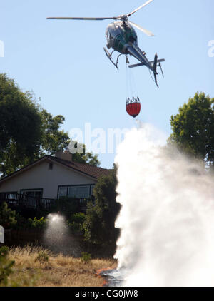 Eine East Bay Regionalparks Hubschrauber als ein Alameda County Sheriff Deputy Wassertropfen (links) hilft mit einem Gartenschlauch wie sie ein Rasen-Feuer in der Nähe von Kemper Grundschule am Mittwoch, 4. Juli 2007, in Castro Valley, Kalifornien reagieren  (Jane Sommerkonzerte/The Daily Review) Stockfoto