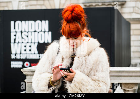 17. September 2012, UK. London Fashionweek im Somerset House, London. Die berühmte und modische besuchen die Shows oder rein zu hängen im Innenhof. Eine Frau mit orange Haare und trägt eine Pelzjacke nutzt ihr Handy Hinweistafel der London Fashion Week. Stockfoto