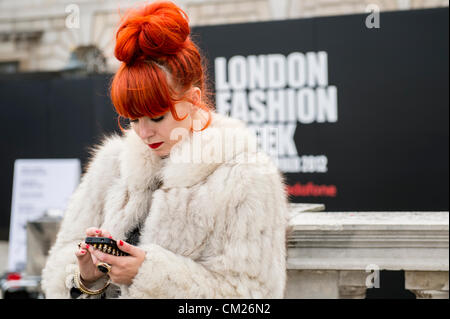 17. September 2012, UK. London Fashionweek im Somerset House, London. Die berühmte und modische besuchen die Shows oder rein zu hängen im Innenhof. Eine Frau mit orange Haare und Fell Jacke verwendet ihr Mobile Hinweistafel der London Fashion Week. Stockfoto