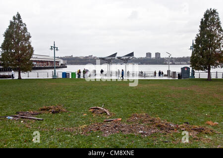 Ablagerungen auf dem Rasen markiert Hochwasser Linie des Hurrikans Sandy Überspannungsschutz im Hudson River Park, wie Menschen in Ferne Promenade mit Blick auf jetzt ruhiger Hudson Fluss entlang spazieren. Dieses Gebiet wurde einen obligatorischen Evakuierung Bereich erklärt. Öffentlicher Verkehrsmittel bleibt geschlossen in New York City & dieser Park ist noch nominell geschlossen. Stockfoto