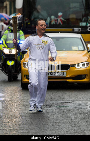 Northampton UK. 2. Juli 2012. Andy Wightman trägt die Olympische Fackel nach unten St Giles Street vor dem Guildhall Northampton Town Center, genauso wie der Regen beginnt. Stockfoto