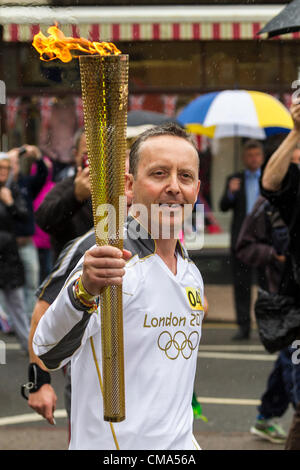 Northampton UK. 2. Juli 2012. Andy Wightman trägt die Olympische Fackel nach unten St Giles Street vor dem Guildhall Northampton Town Center, genauso wie der Regen beginnt. Stockfoto